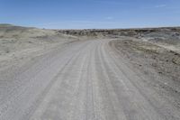 a dirt road is surrounded by some hills and desert like terrain as the vehicle sits on it