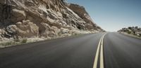 an empty highway with no traffic on both sides of it in the desert area with rocks and grass