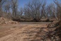 a dirty, dirt road with a river behind it and trees around the intersection behind