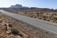 a man rides a motorcycle down a desert road near rocks and shrubs on both sides