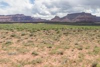 a desert landscape with mountains in the background in front of clouds and blue sky with some patches of grass