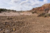 rocky terrain with sparse shrubs and rocks below, on an overcast day with blue sky and white clouds