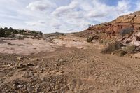 rocky terrain with sparse shrubs and rocks below, on an overcast day with blue sky and white clouds