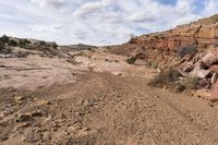 rocky terrain with sparse shrubs and rocks below, on an overcast day with blue sky and white clouds