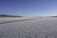 the tire track of two cars parked on a vast flat terrain desert landscape with mountains in the background