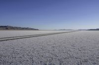 the tire track of two cars parked on a vast flat terrain desert landscape with mountains in the background