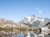 a person is hiking on a trail in the mountains overlooking water and rocks with snow capped mountains