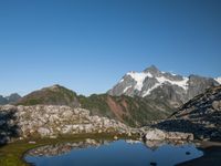 a person is hiking on a trail in the mountains overlooking water and rocks with snow capped mountains