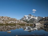 a person is hiking on a trail in the mountains overlooking water and rocks with snow capped mountains