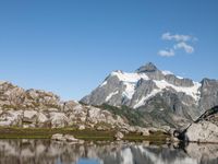 a person is hiking on a trail in the mountains overlooking water and rocks with snow capped mountains