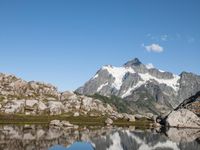 a person is hiking on a trail in the mountains overlooking water and rocks with snow capped mountains