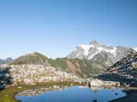 a person is hiking on a trail in the mountains overlooking water and rocks with snow capped mountains