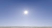 two people sitting on top of a snow covered field under a bright sun flares in the distance