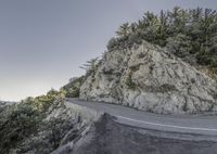 a motorcyclist rides down the road below an icy cliff face while surrounded by trees