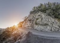 a motorcyclist rides down the road below an icy cliff face while surrounded by trees