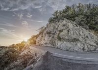 a motorcyclist rides down the road below an icy cliff face while surrounded by trees