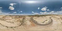 a very big winding road in the desert with mountains and clouds in the sky, shot through fisheye lens