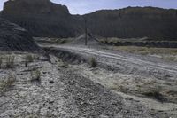 a truck parked in front of a mountain on a gravel road near a telephone pole