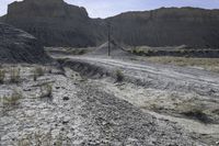 a truck parked in front of a mountain on a gravel road near a telephone pole