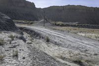 a truck parked in front of a mountain on a gravel road near a telephone pole