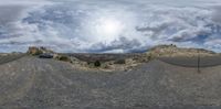 some cars and a building on a mountain top area and clouds in the sky and a sun over them