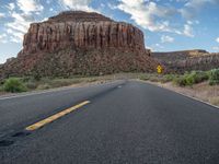 a empty road next to a rock covered mountain side on a cloudy day in the desert