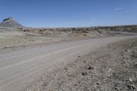 a dirt road is surrounded by some hills and desert like terrain as the vehicle sits on it