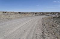 a dirt road is surrounded by some hills and desert like terrain as the vehicle sits on it