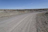 a dirt road is surrounded by some hills and desert like terrain as the vehicle sits on it