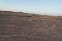 a lone dirt hill with a large rock in the distance in the middle of the barren plain