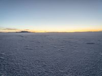 the snow is white with many footprints in it at sunset above mountains, but at dusk there are mountains in the distance