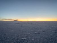 the snow is white with many footprints in it at sunset above mountains, but at dusk there are mountains in the distance