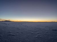 the snow is white with many footprints in it at sunset above mountains, but at dusk there are mountains in the distance