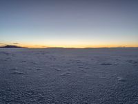 the snow is white with many footprints in it at sunset above mountains, but at dusk there are mountains in the distance