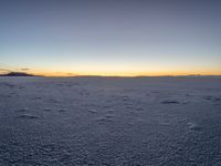 the snow is white with many footprints in it at sunset above mountains, but at dusk there are mountains in the distance