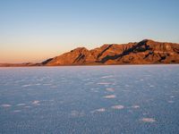 a small hill in the middle of snow covered plain of water and sky on a clear day