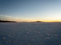 an empty snow - covered landscape with blue and white skies and low sun setting over the ocean