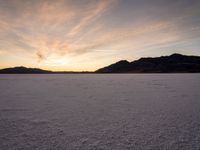 a large snowy area with many tracks and tracks on the ground at sunset time and hills behind it