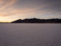 a large snowy area with many tracks and tracks on the ground at sunset time and hills behind it