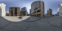 the spherical photo captures a park with people riding bicycles in the background and buildings in the distance