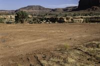 dirt and rocks with an open field and hills in the distance behind it, a man on a motorcycle