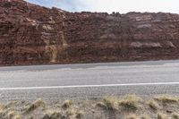 a motorcycle parked on the side of a highway near a cliff face covered with a mountain