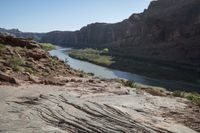 two people on their motorcycle on the rocky road next to the river while a horse stands at the edge