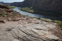 two people on their motorcycle on the rocky road next to the river while a horse stands at the edge