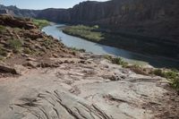 two people on their motorcycle on the rocky road next to the river while a horse stands at the edge