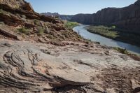 two people on their motorcycle on the rocky road next to the river while a horse stands at the edge