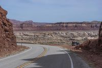 a motorcycle travels down the road between some rocks and the desert plain in arizona, usa