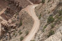 a road with three cars going down a narrow path in the mountains beside a cliff