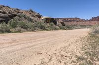 a dirt road near some cliffs and brushs with no cars in sight on it