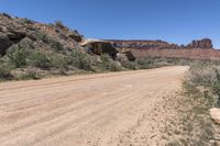 a dirt road near some cliffs and brushs with no cars in sight on it